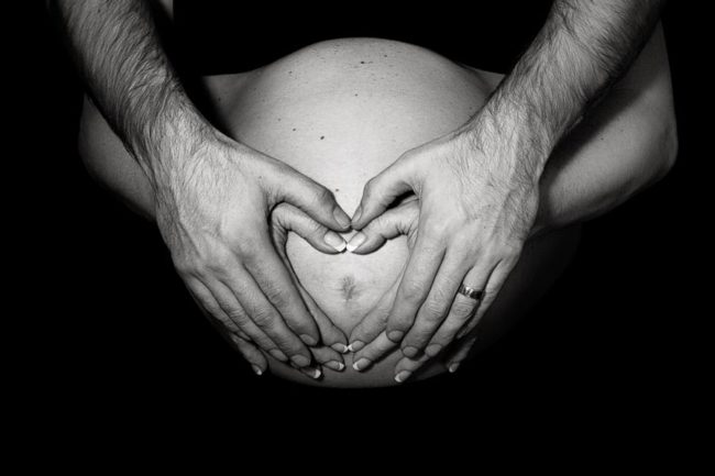 Couple's hands forming a heart on belly